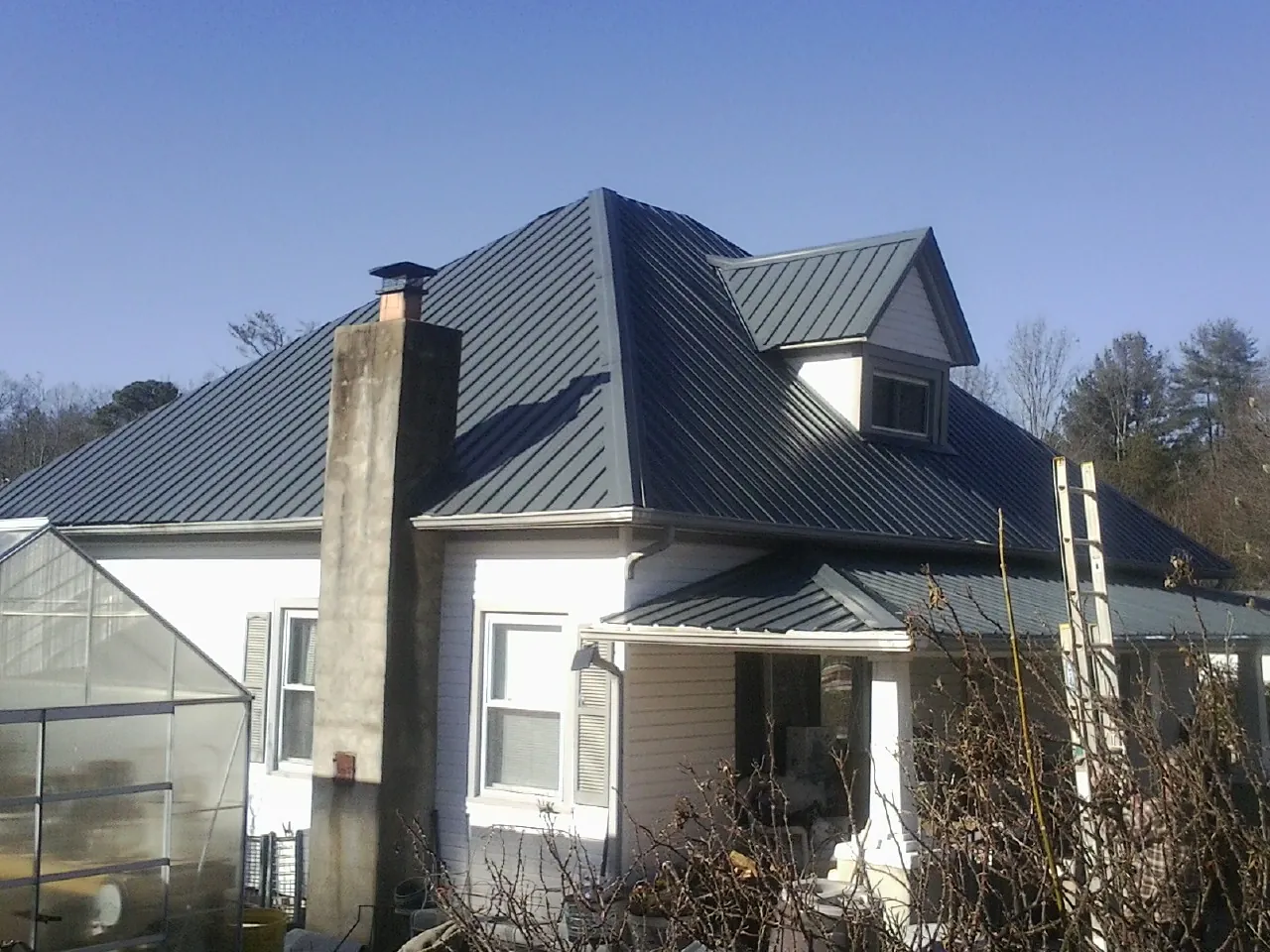 Dark blue standing seam metal roof on a white farmhouse with dormer — Slate & Tile Roof Repair by Roofing Brothers in Cataumet