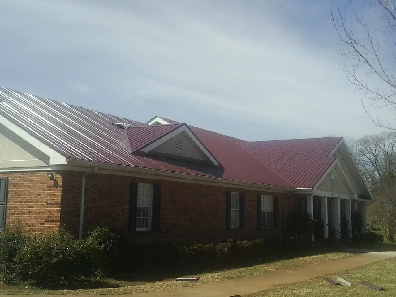 Red metal roof with gabled entries on a long brick building, from a Hail Damage Roof Repair job in Cataumet