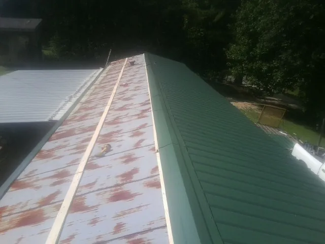 Old rusted panels beside newly installed green metal roofing — Wind Damage Roof Repair by Roofing Brothers in Cataumet
