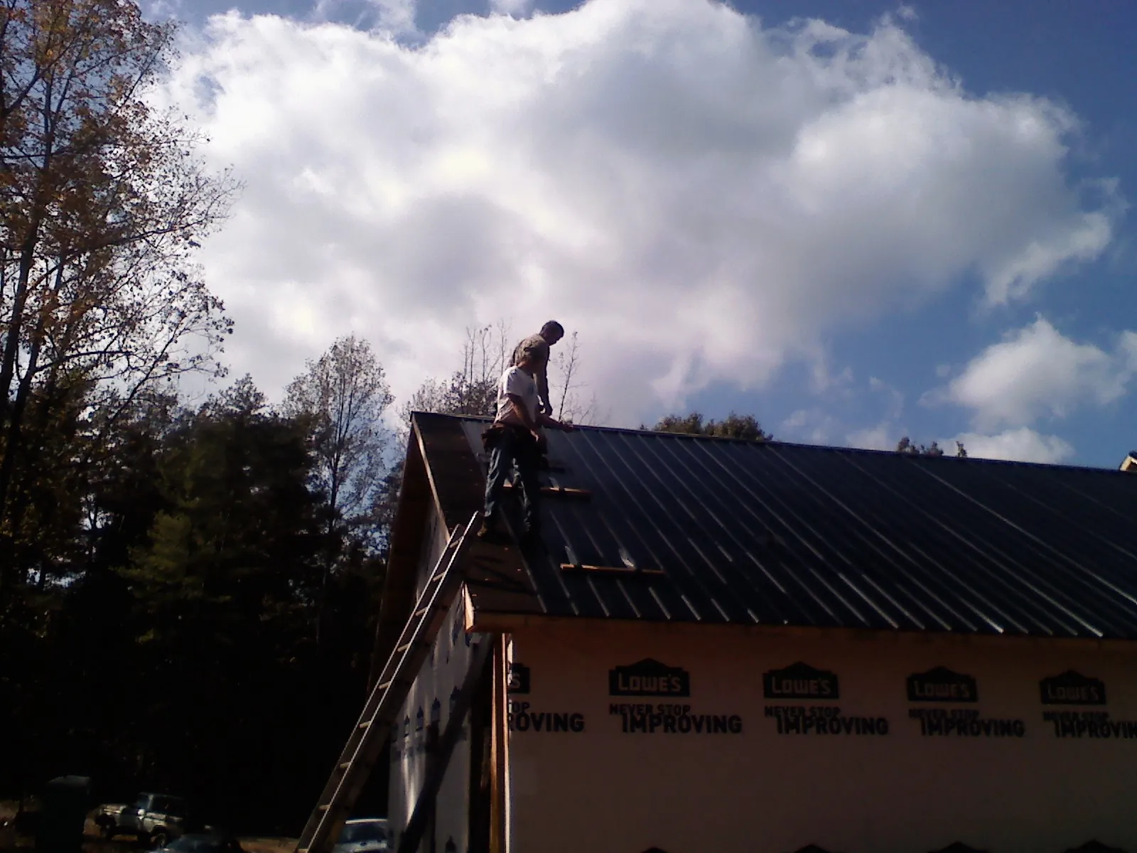 Roofer fastening dark metal panels high against a cloudy sky, from a Roof Inspection job in Cataumet