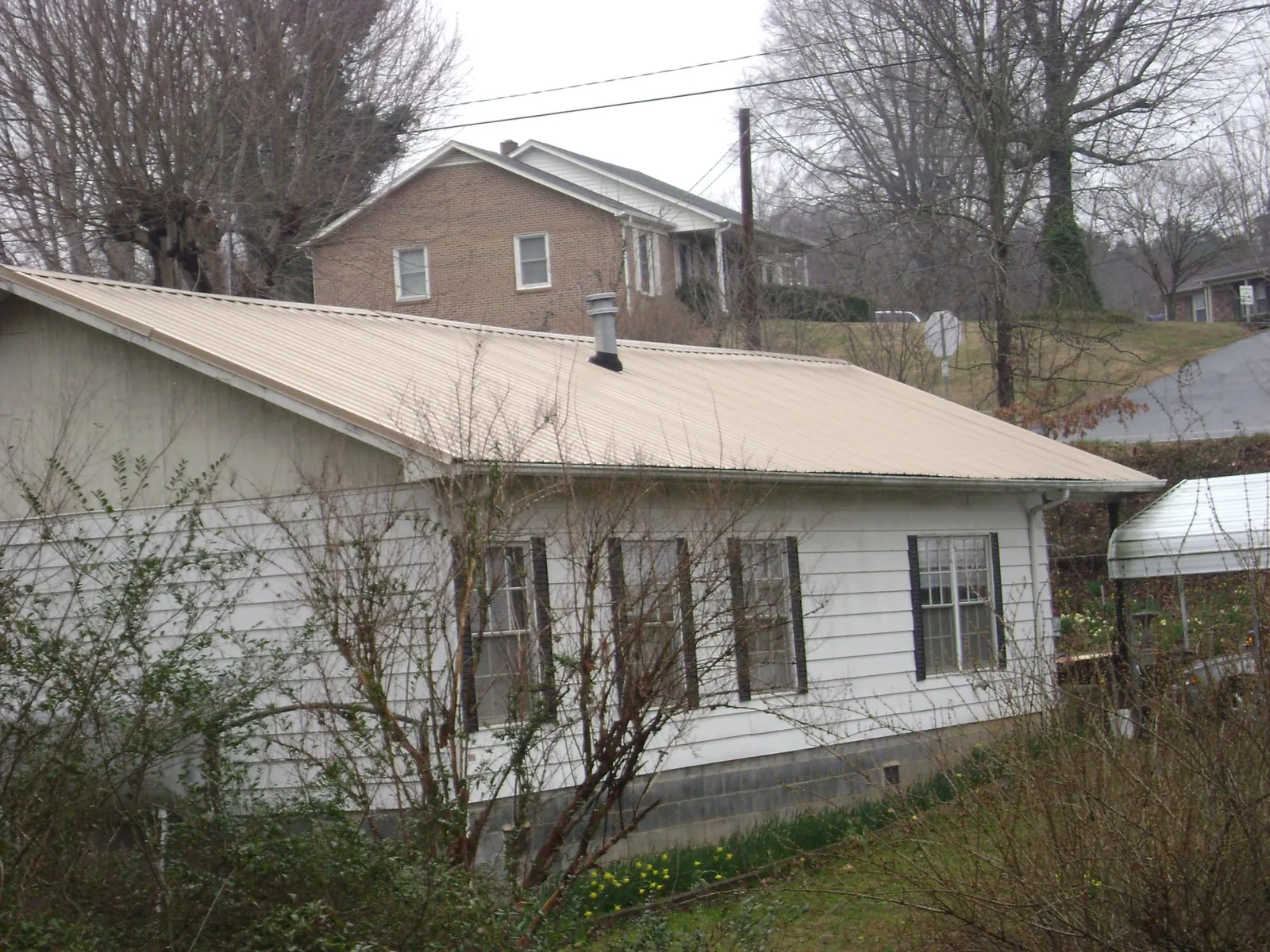 Tan metal roof on a white sided house set into a hillside — Commercial Roofing by Roofing Brothers in Cataumet
