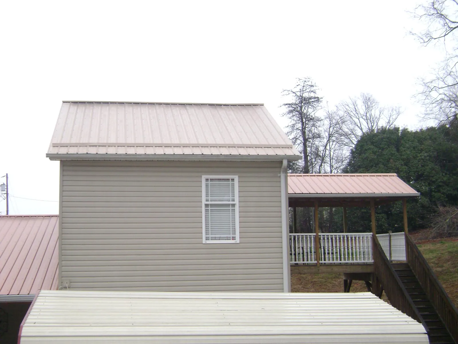 Tan metal roofs on a two story addition and attached porch, from a Roof Replacement job in Cataumet