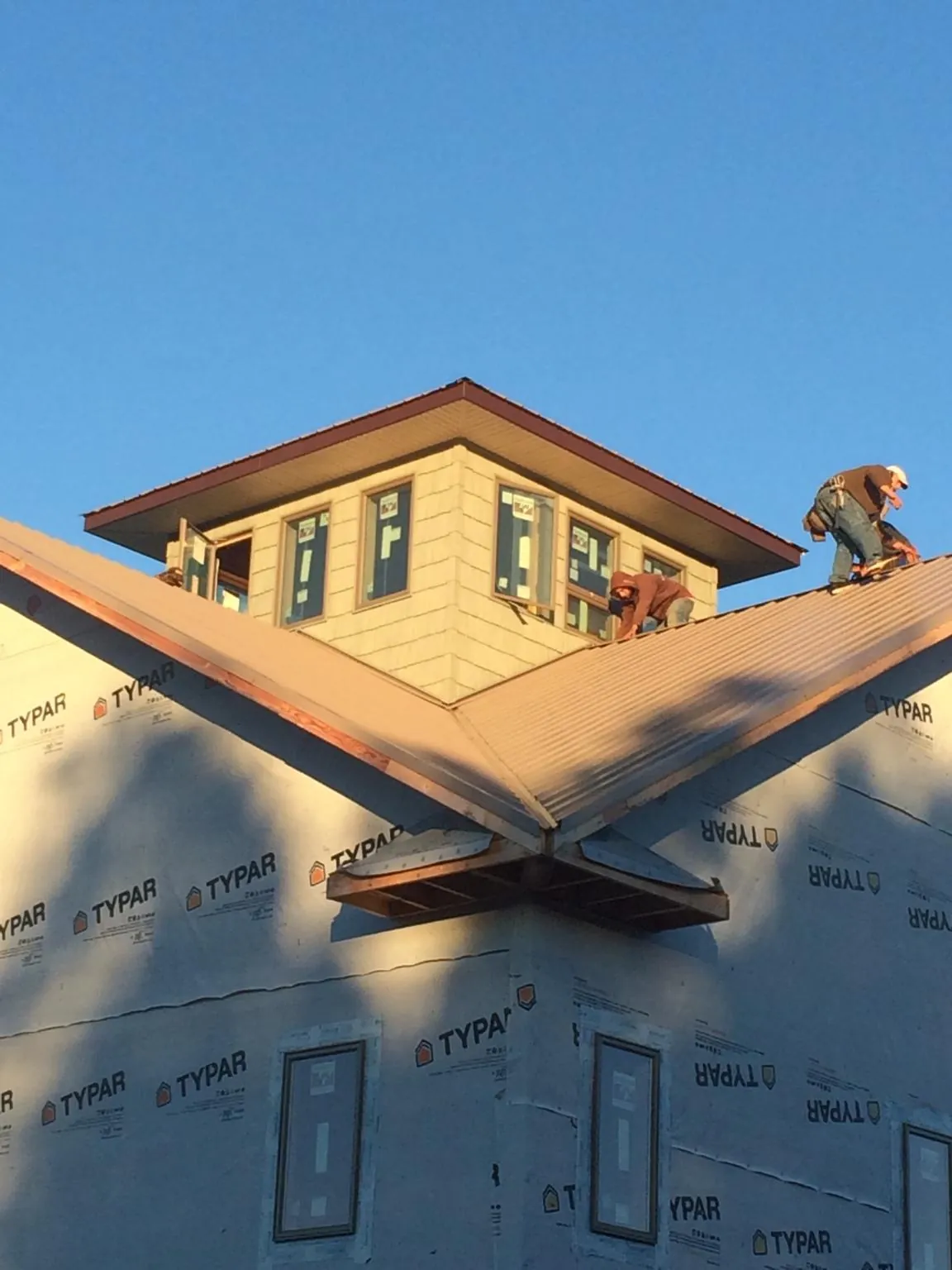 Roofers working around a rooftop cupola on a new metal roof at sunset — Roof Waterproofing in Cataumet by Roofing Brothers